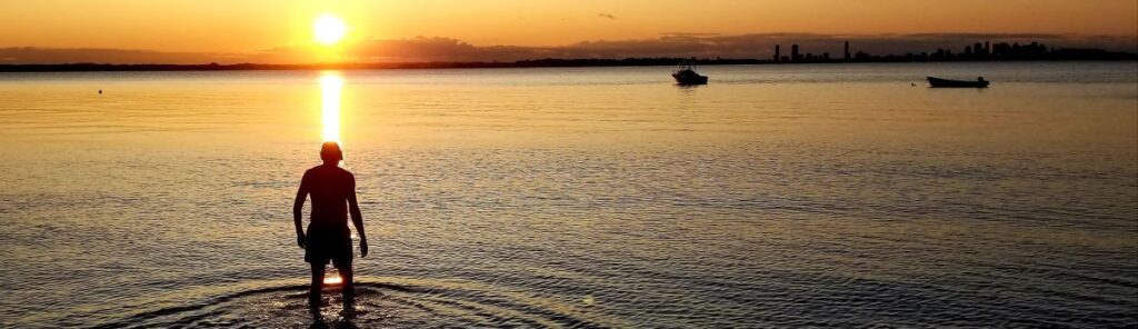 Figure standing in open water at sunset